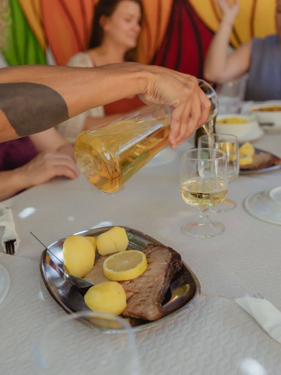 A hand pouring white wine into a glass that sits on a table with food.