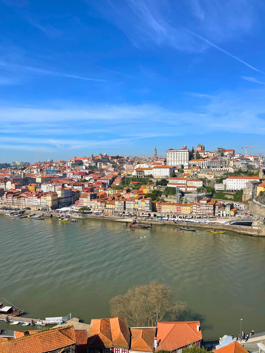 Porto, Portugal, in August: a scenic view of colorful hillside buildings along the Douro River under a bright blue sky.