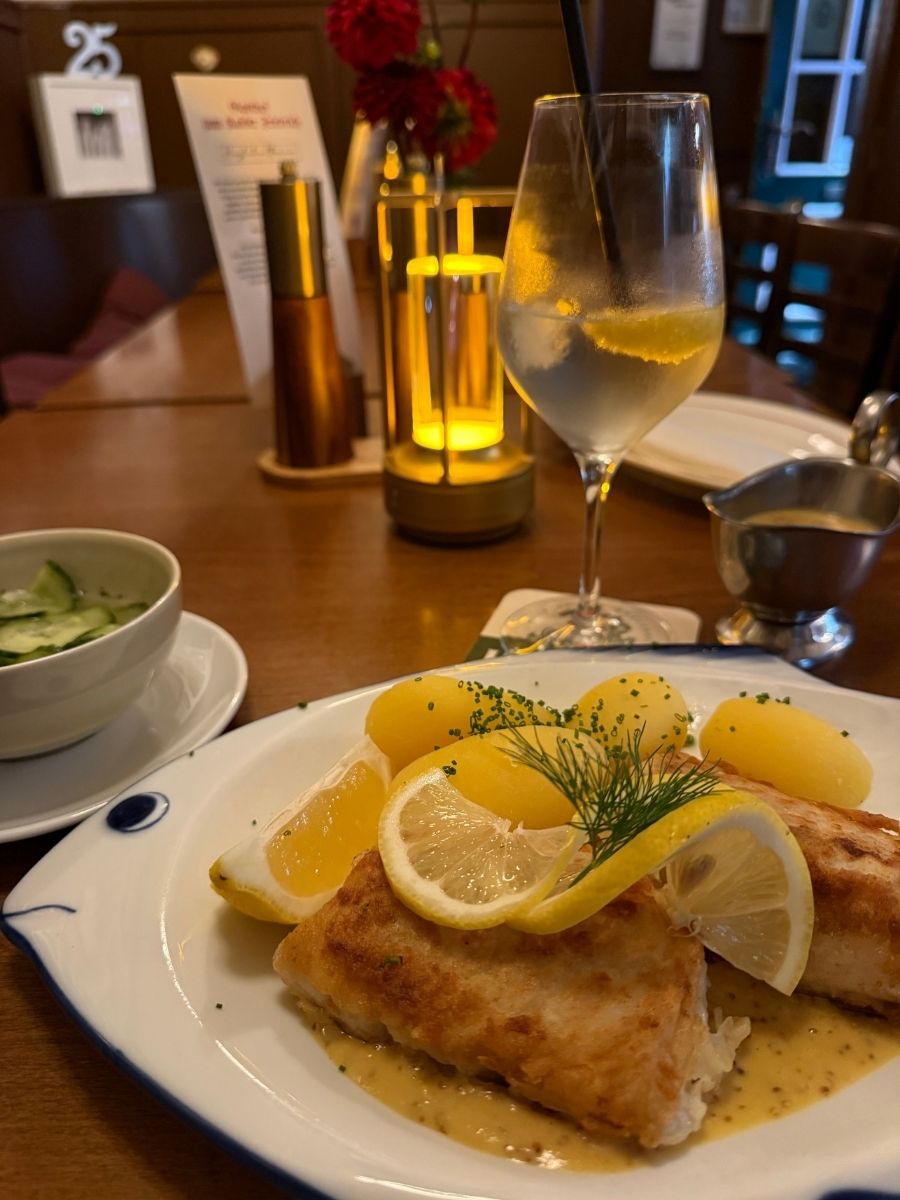 Crispy fried fish with potatoes, lemon, and mustard sauce, enjoyed at a cozy Bremen restaurant with a refreshing drink.