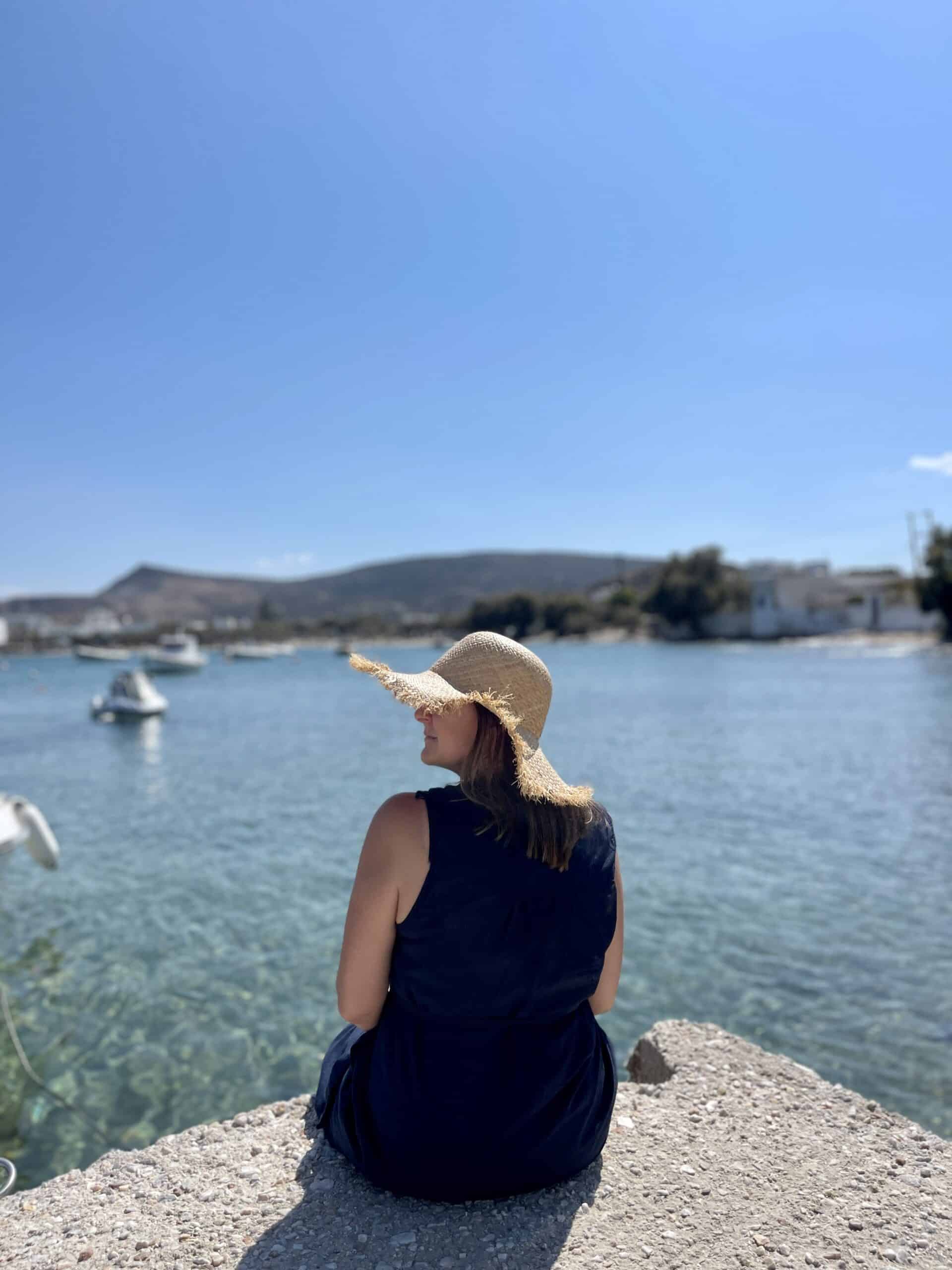 A Woman sitting on the edge of a walk way in front of the ocean