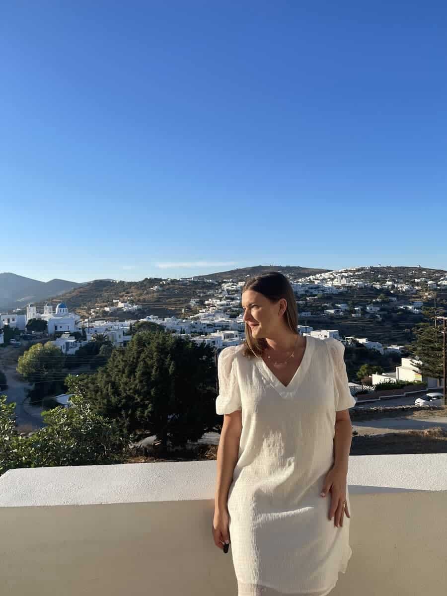 A woman in a white dress on a balcony with the mountains and village behind her