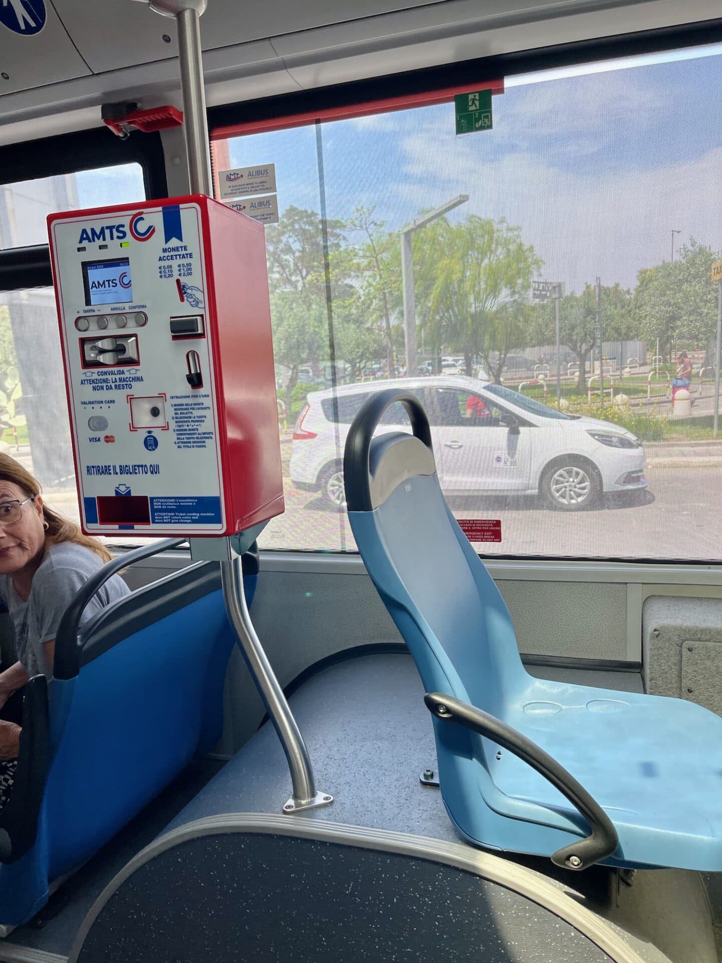 Inside a bus in Catania with an AMTS ticket validation machine and a view of a street outside the window.
