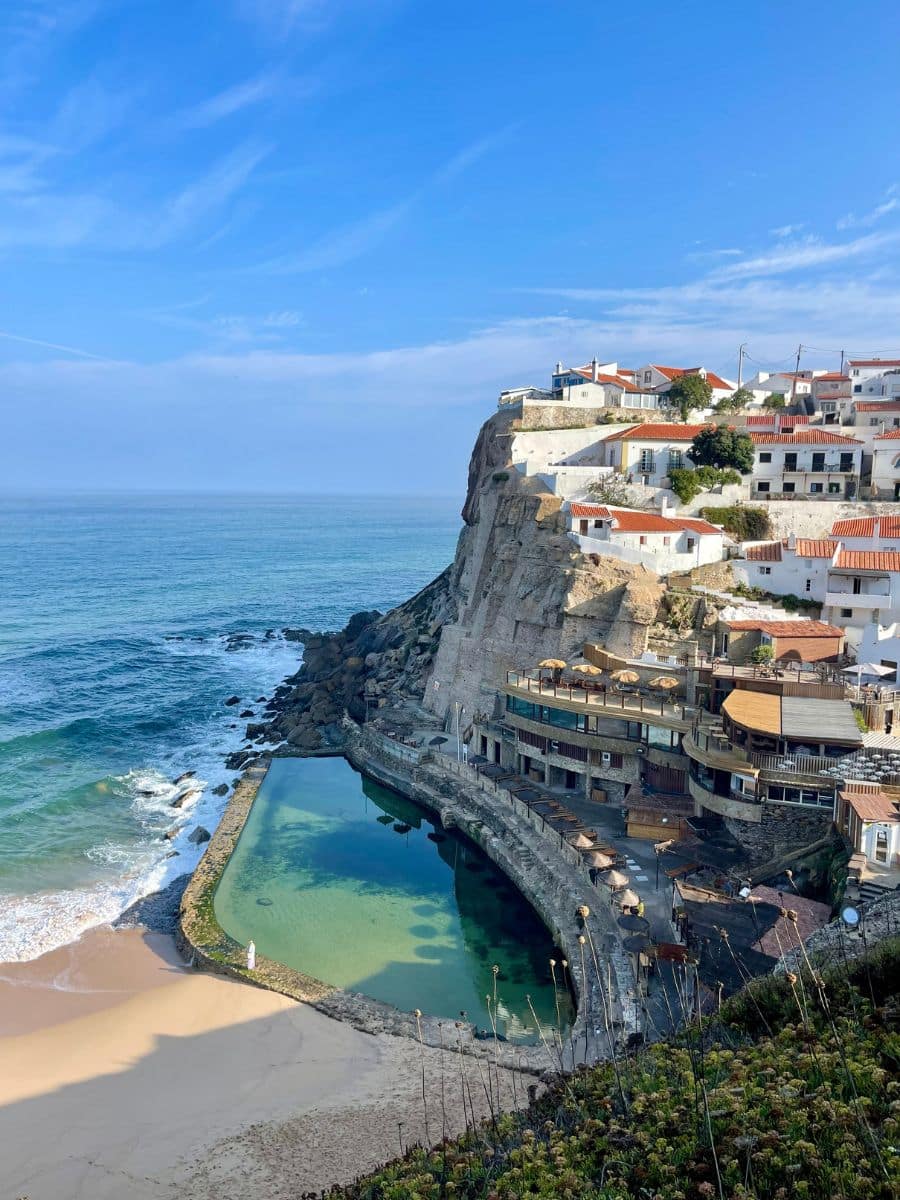 Breathtaking aerial view of the natural ocean pool nestled beneath cliffs and white houses in the picturesque village of Azenhas do Mar.