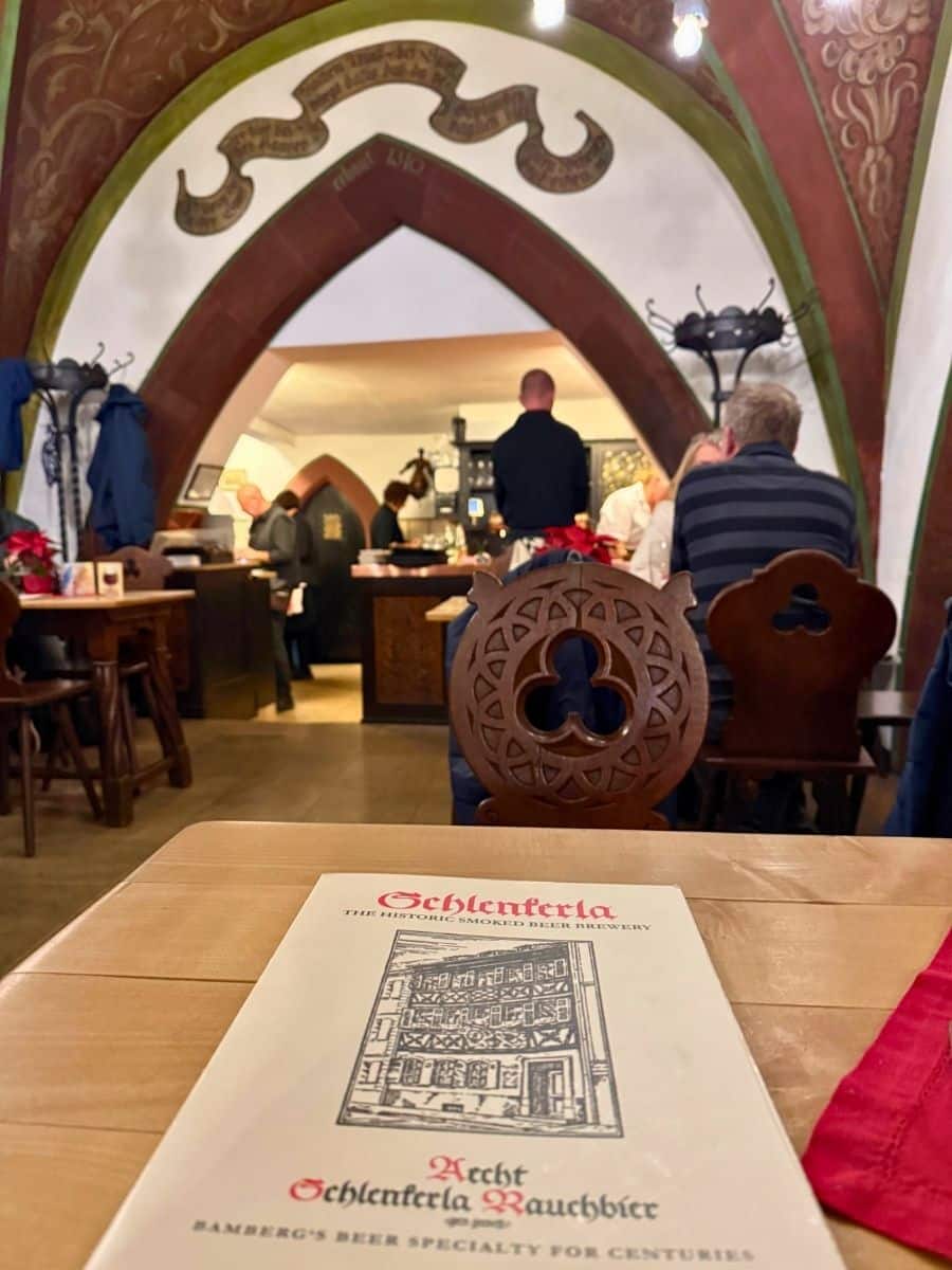 Interior view of the traditional Schlenkerla tavern in Bamberg, featuring Gothic archways, decorative ceiling art, and diners seated in a cozy atmosphere.