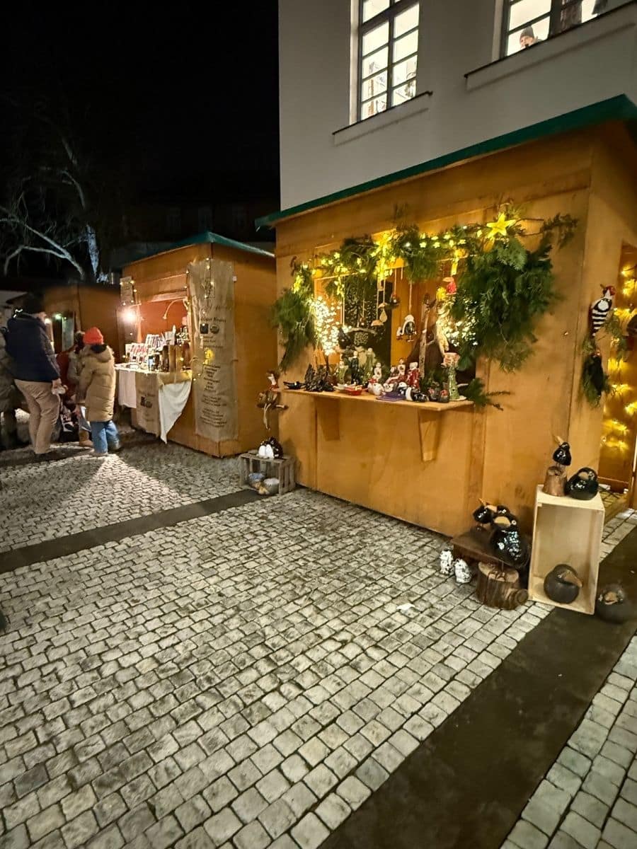 Evening scene at a Christmas market in Bamberg with cozy wooden stalls decorated with garlands, lights, and handmade crafts.