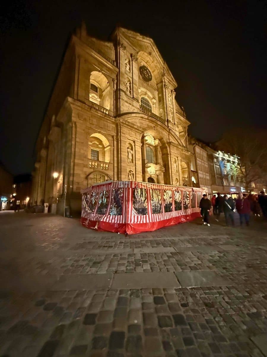Illuminated historic church in Bamberg at night with a large red-and-white striped tent set up in front during the holiday festivities.
