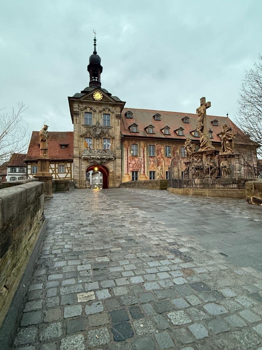 Front view of Bamberg’s iconic Old Town Hall (Altes Rathaus) with its detailed façade, cobblestone bridge, and statue group under a cloudy winter sky.