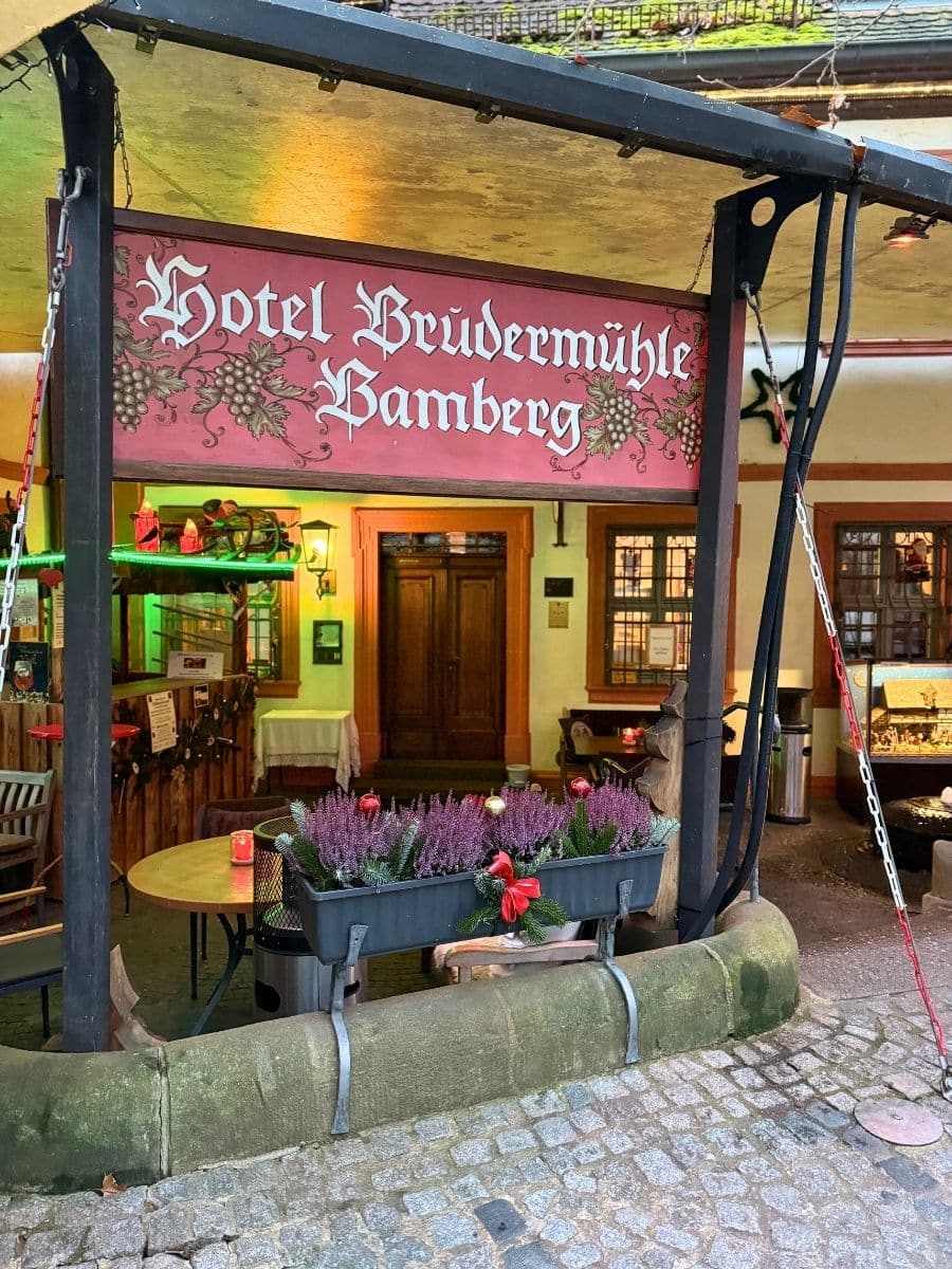 Festive entrance of Hotel Brudermühle in Bamberg, with holiday decorations and outdoor seating under a canopy.