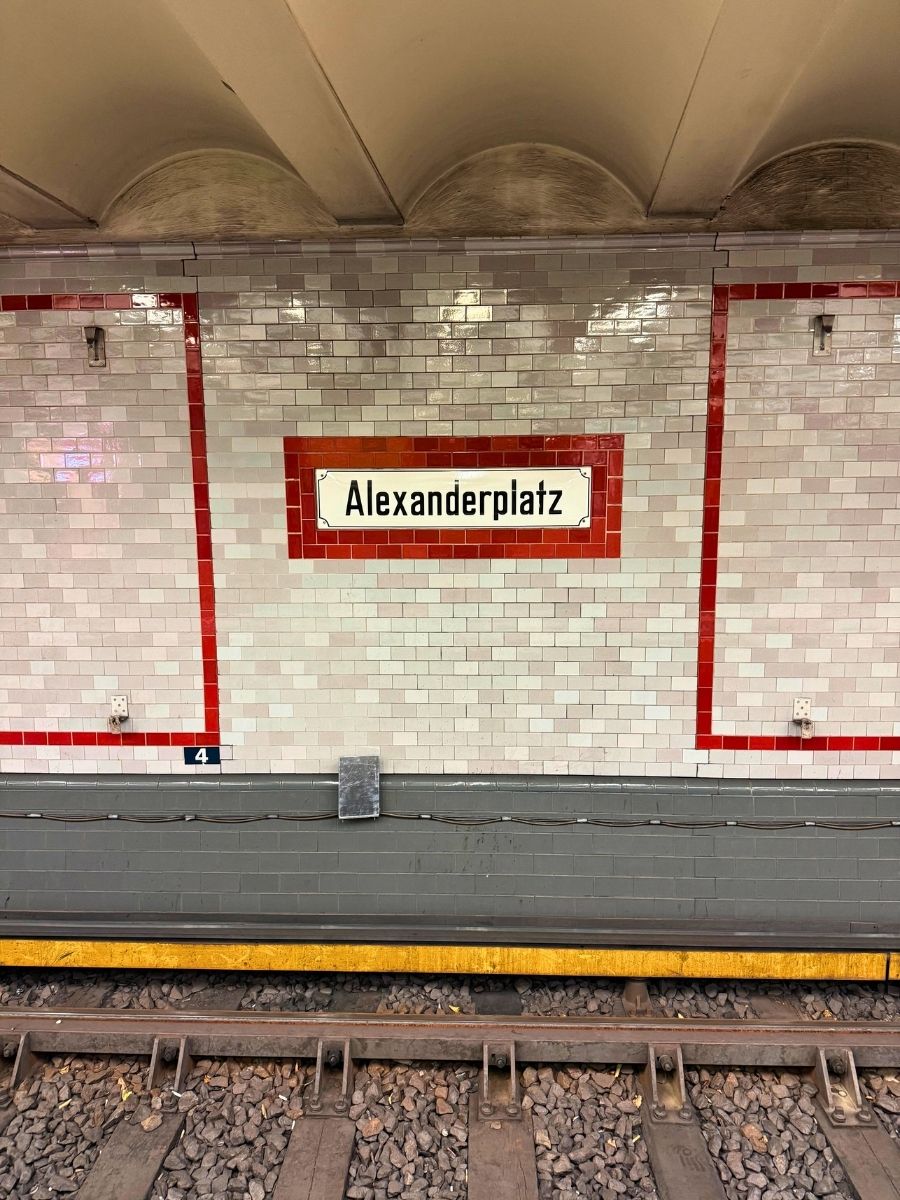 Alexanderplatz U-Bahn station platform in Berlin with tiled walls and train tracks in the foreground.