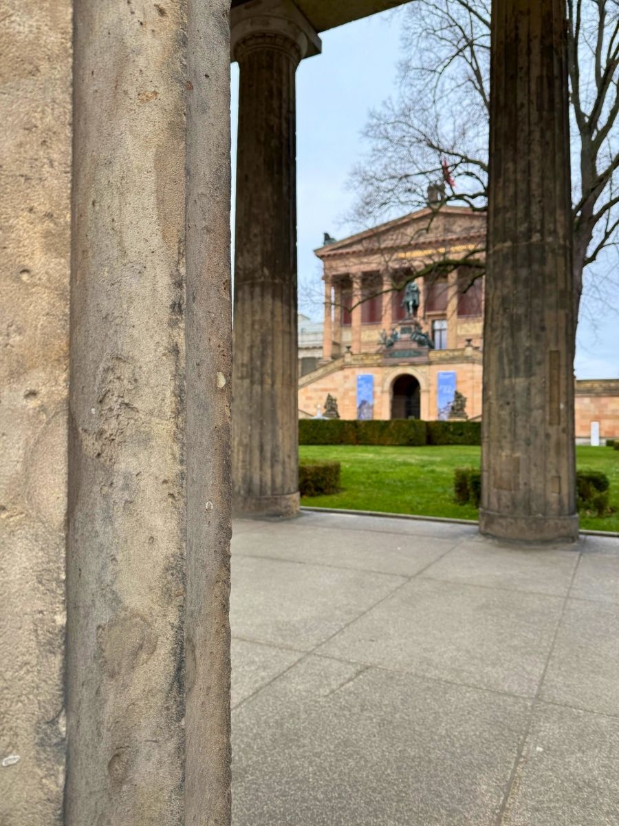 View through ancient stone columns on Museum Island in Berlin, framing a historic museum building in the distance.