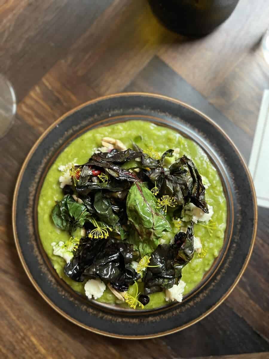 An elegantly plated dish of risotto with vibrant green sauce, topped with dark sautéed mushrooms and garnished with herbs, served in a Copenhagen dining establishment.