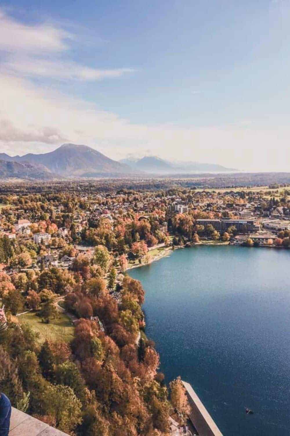 Winter view of the medieval Bled Castle perched atop a steep cliff overlooking the calm waters of Lake Bled, a popular winter destination for history enthusiasts.