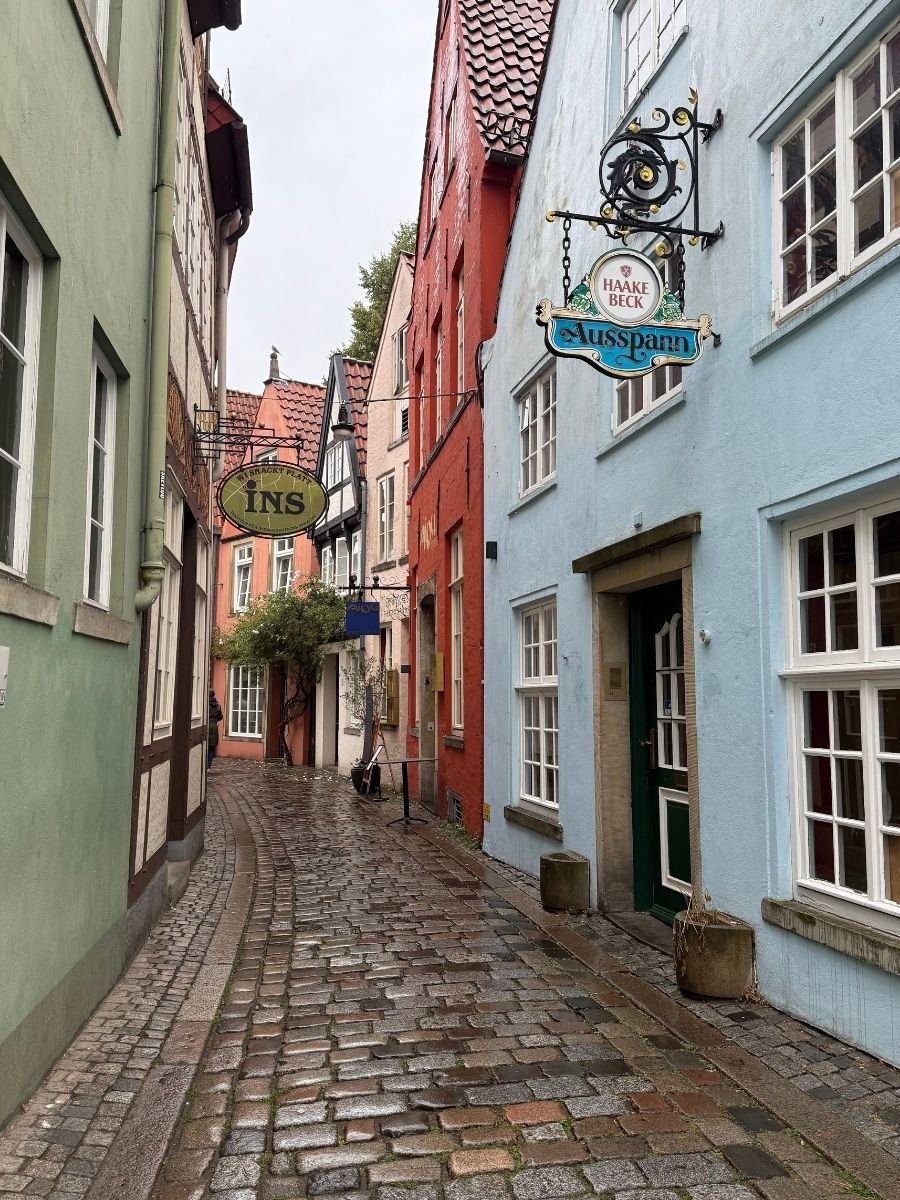 Narrow cobblestone street lined with colorful houses and pub signs in the Schnoor quarter of Bremen.