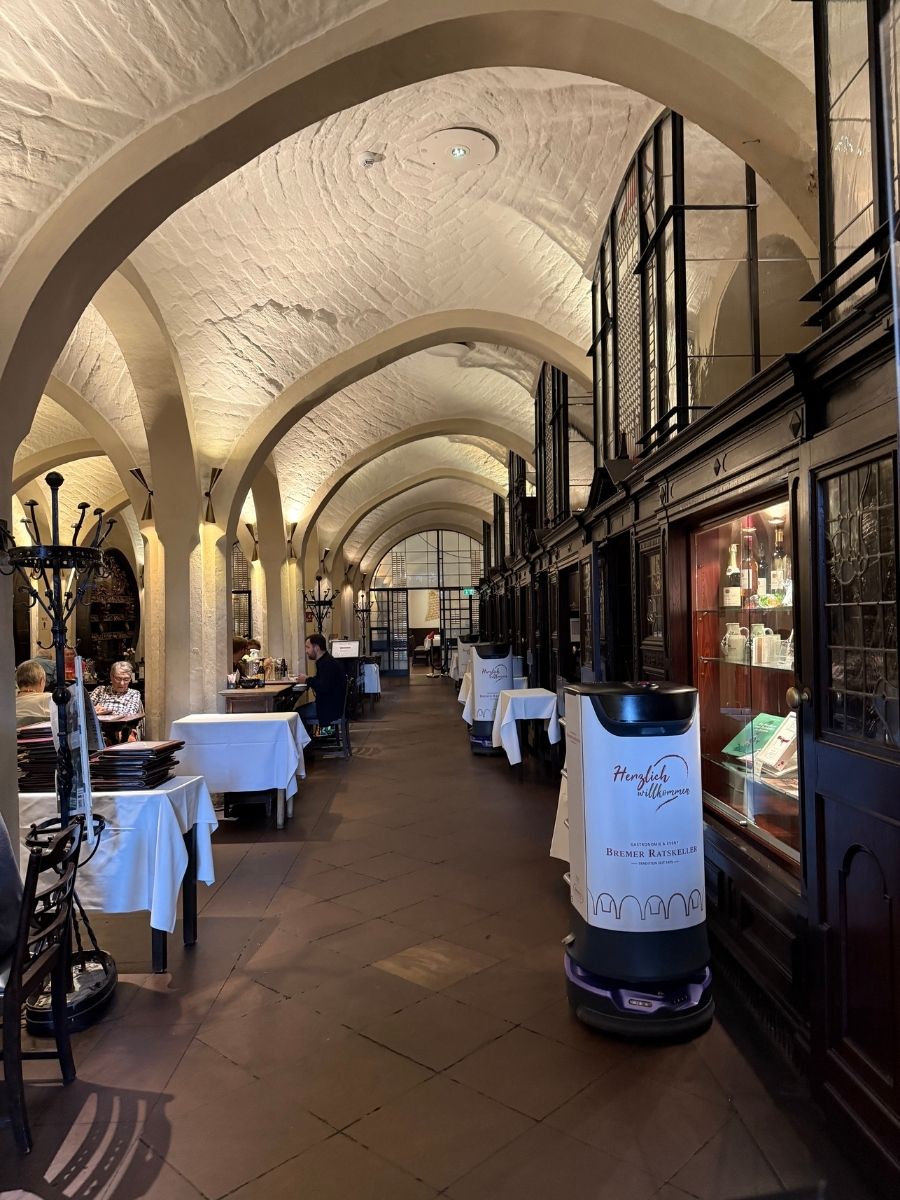 Historic vaulted dining hall in Bremen with arched ceilings, dark wood cabinets, and white-covered tables.