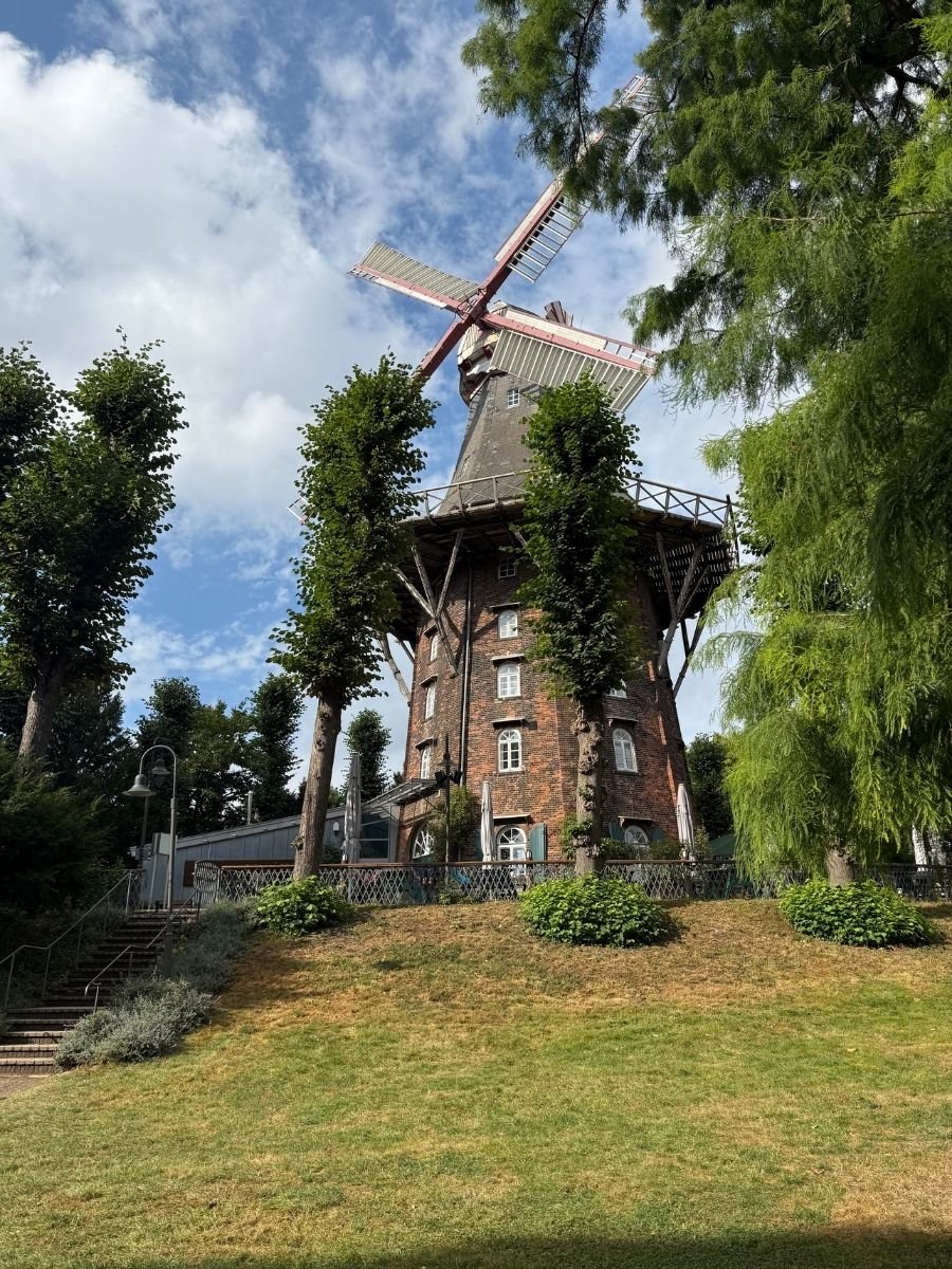 Historic windmill surrounded by greenery and trees under a blue sky in Bremen, Germany.
