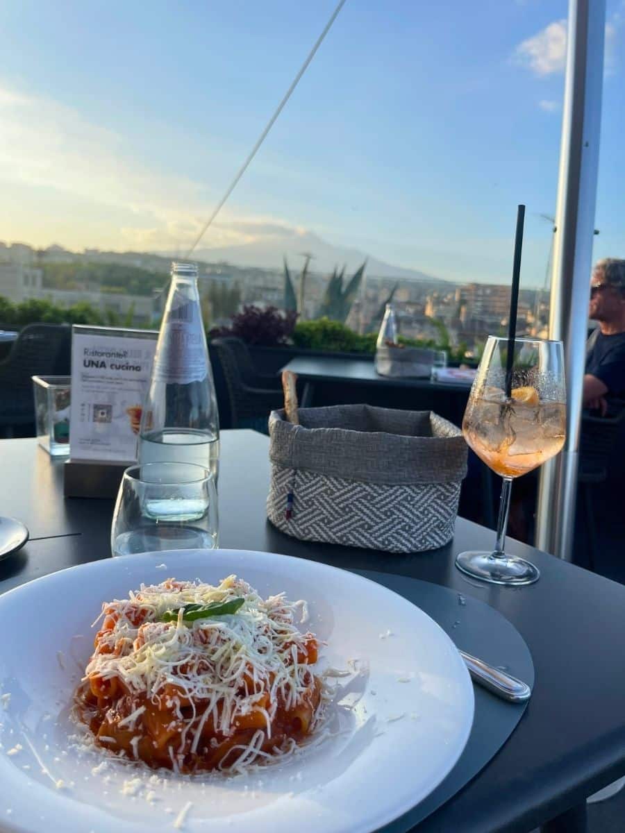 A plate of pasta topped with grated cheese at a rooftop restaurant in Catania, with Mount Etna visible in the background.