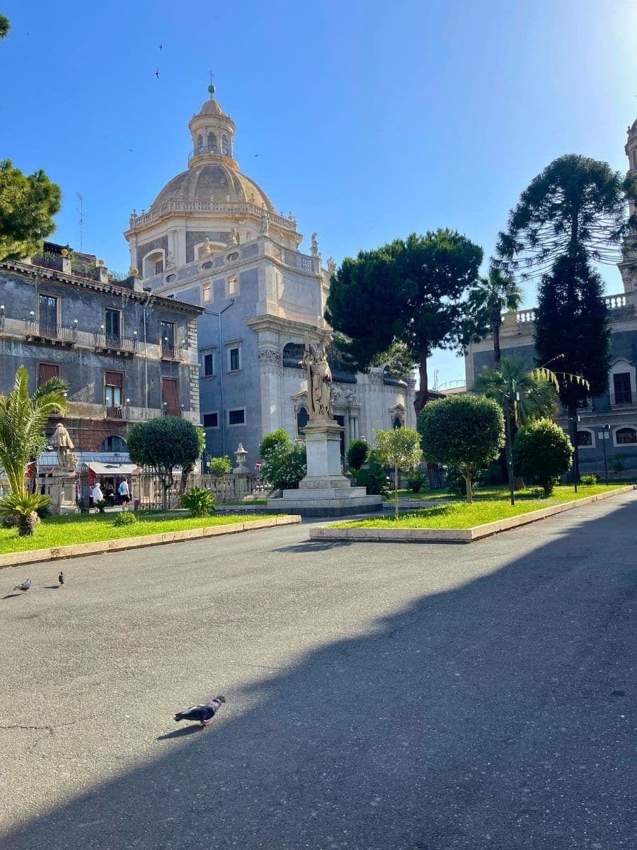 A wide shot of Piazza del Duomo in Catania, Sicily, showcasing the architectural grandeur of the Catania Cathedral and the playful Elephant Fountain with its obelisk.
