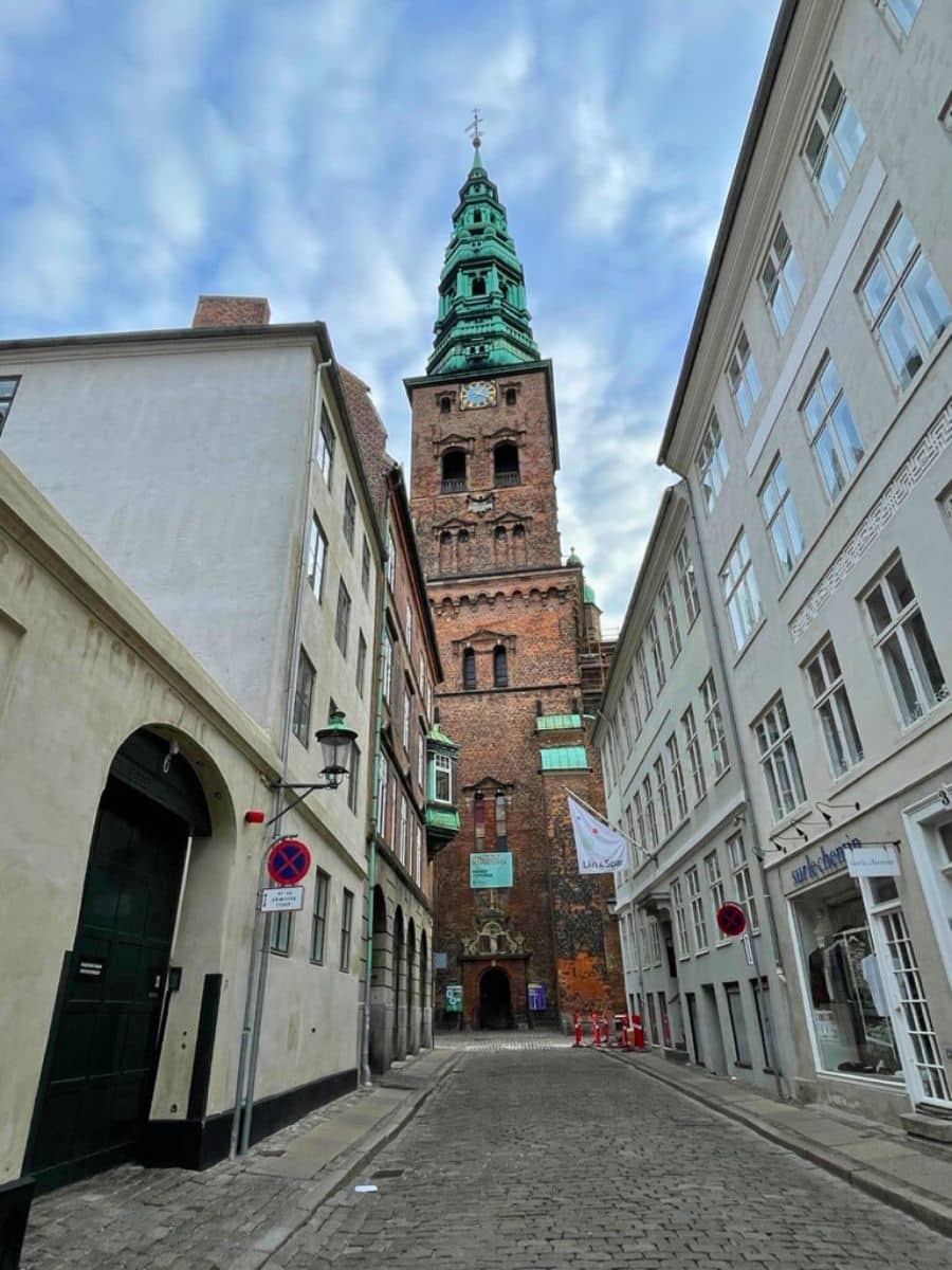 Narrow cobblestone street leading to the intricate green spire of St. Nikolaj Church in Copenhagen, showcasing the city’s rich history and architectural heritage.