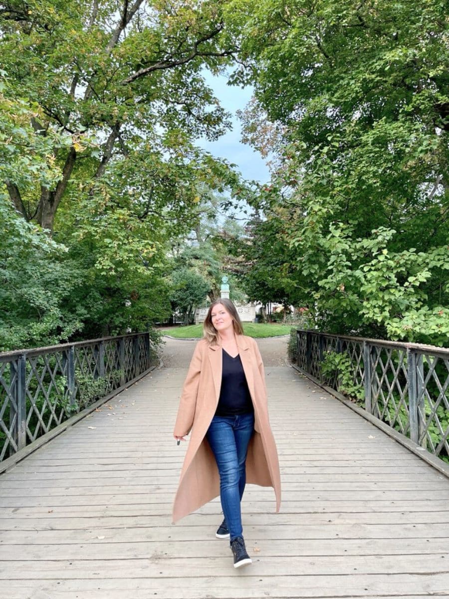 A woman walking on a wooden bridge in a serene park in Copenhagen, surrounded by lush green trees and shrubbery, exemplifying the city's tranquil and safe atmosphere.