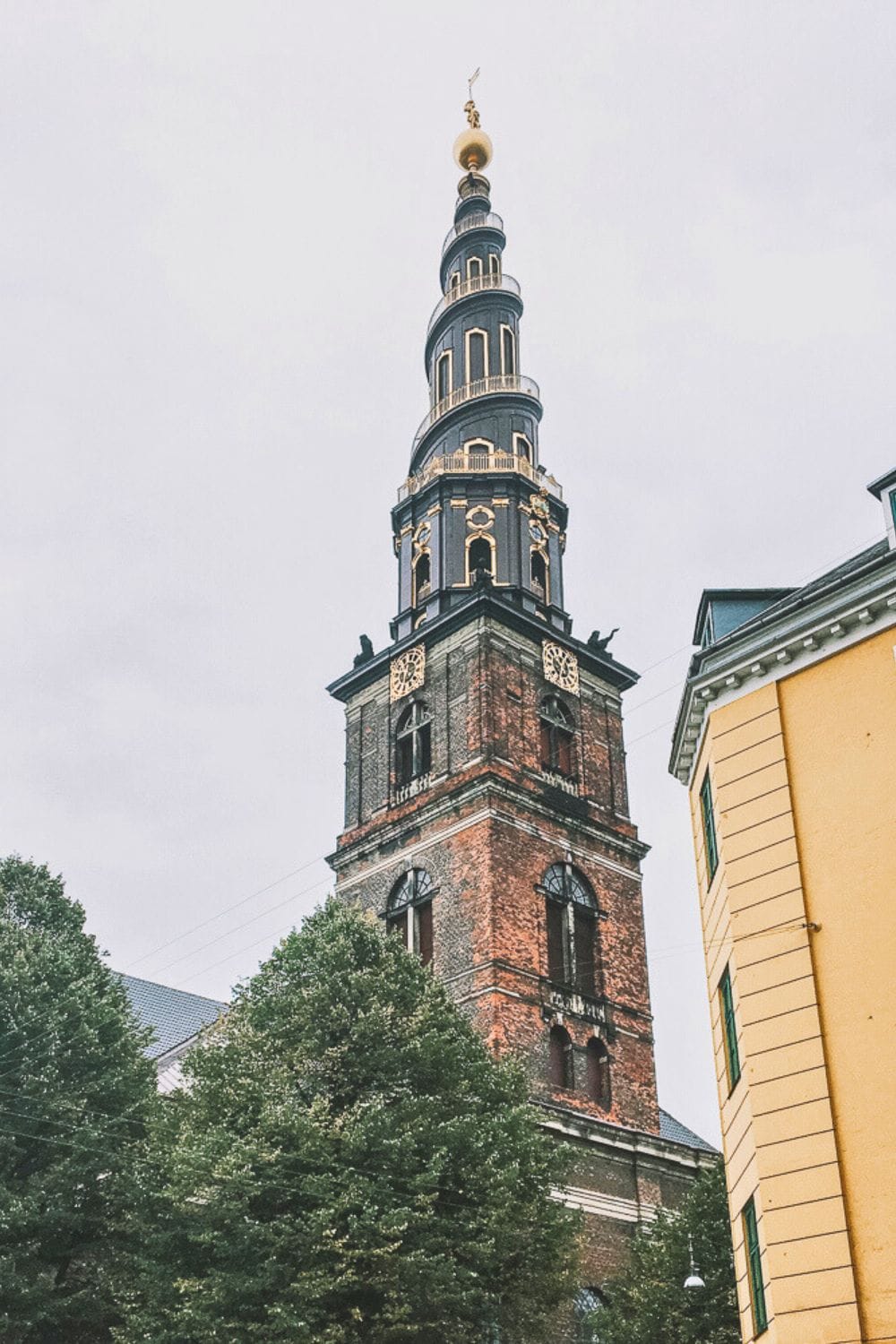 A view of the iconic spiral spire of the Church of Our Saviour in Copenhagen, Denmark, framed by historic buildings.