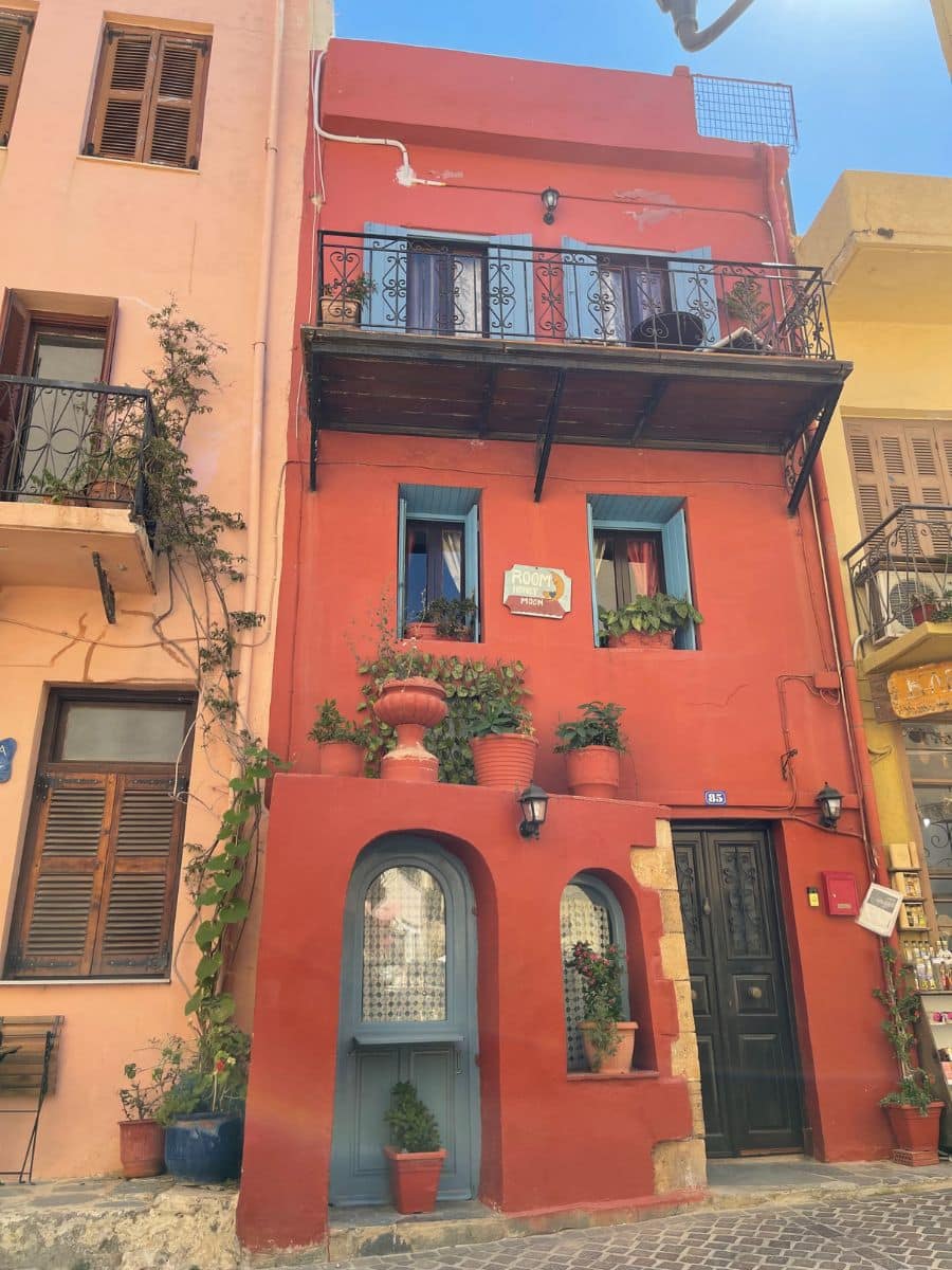 A vibrant red building adorned with potted plants and flowers in Chania, reflecting the charming and colorful architecture of Crete.