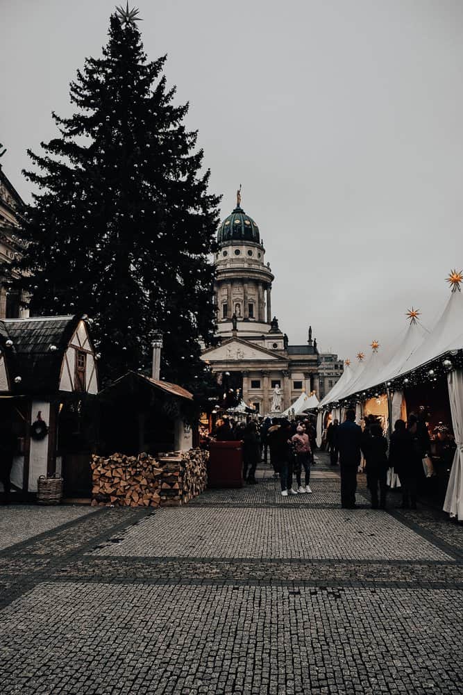 A picturesque view of a Berlin Christmas market, set against the backdrop of the grand Gendarmenmarkt cathedral, featuring festive stalls and visitors enjoying the atmosphere.