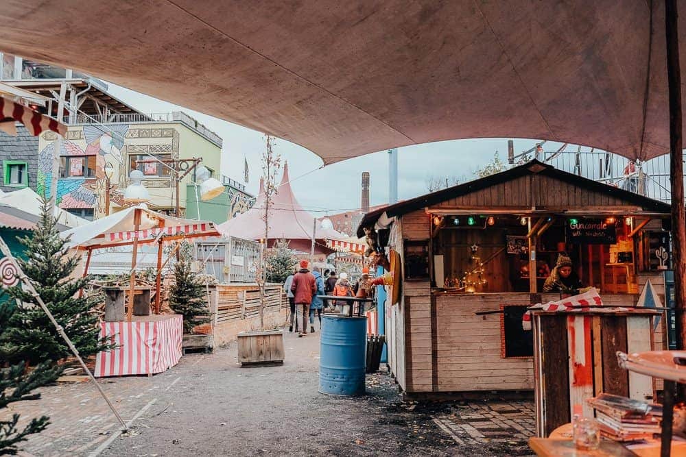 A lively open-air Christmas market in Berlin, featuring colorful stalls and canopies, where visitors are seen mingling and exploring festive offerings.