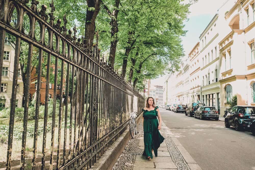 Confident woman in a flowing green dress walking alone on a tree-lined Berlin street, exemplifying the empowerment of solo travel