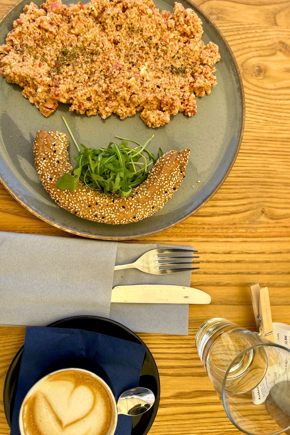A healthy Mediterranean breakfast on a wooden table, with scrambled eggs on a sesame bagel and a heart-shaped latte, ready to start a day in Hydra