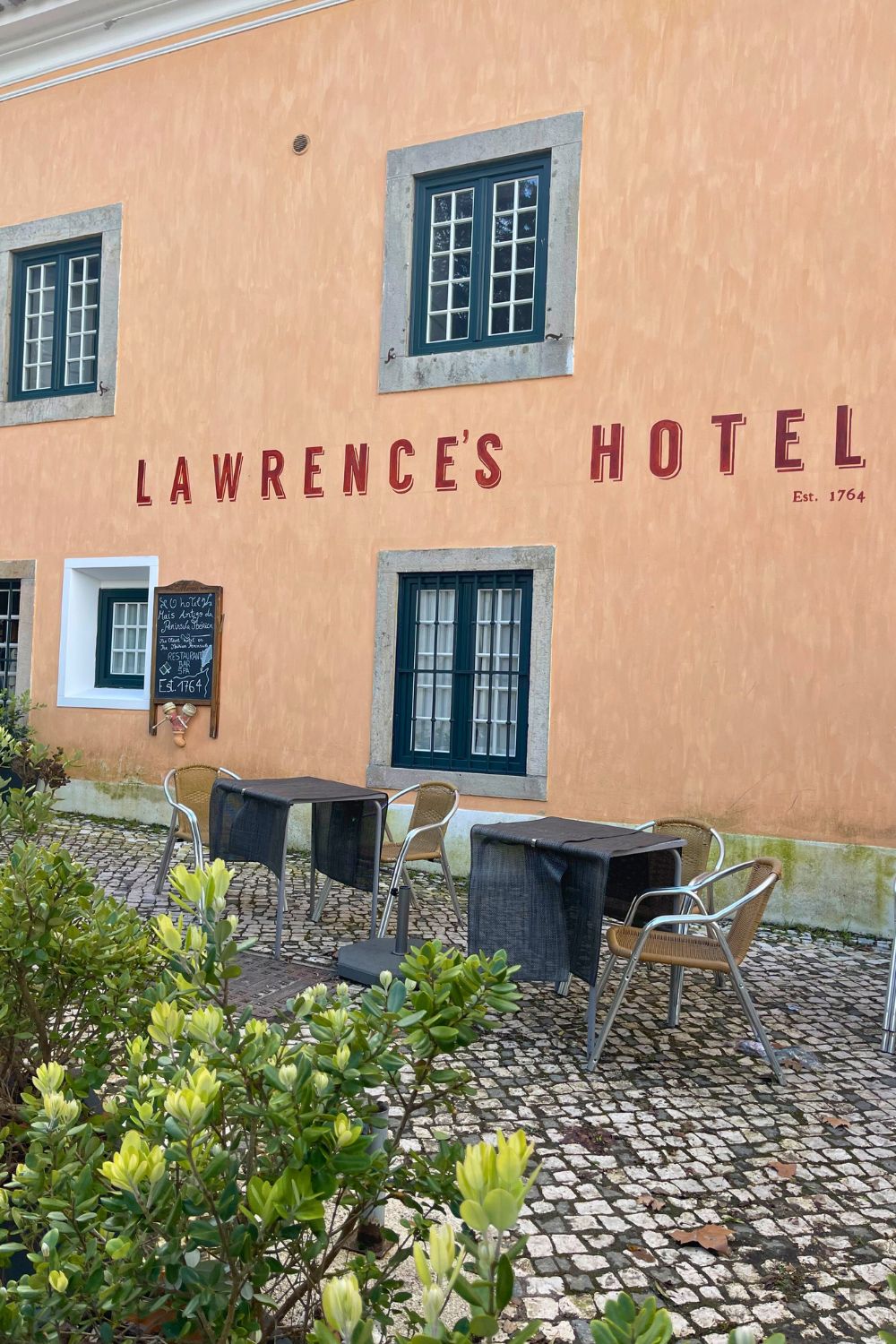 The exterior of Lawrence's Hotel in Sintra, featuring a warm peach-colored facade with vintage-style windows and outdoor seating on a cobblestone patio.