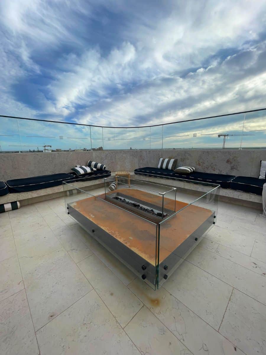 Outdoor seating area with a glass fire pit and striped cushions overlooking Faro.