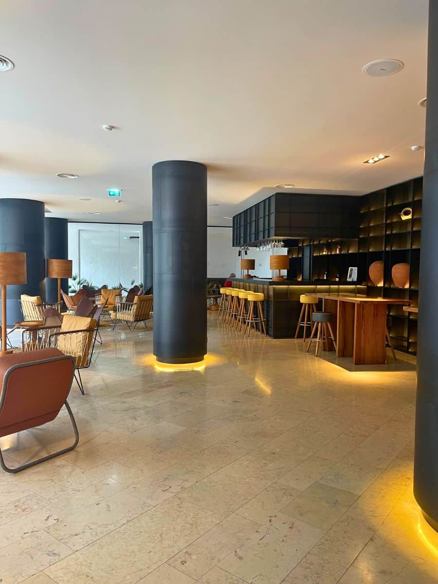 Stylish seating area with warm lighting, wooden accents, and a bar in the 3HB Faro hotel lobby.