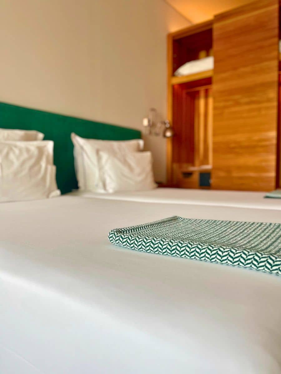 Neatly made twin beds with white linens and green accents in 3HB Faro.