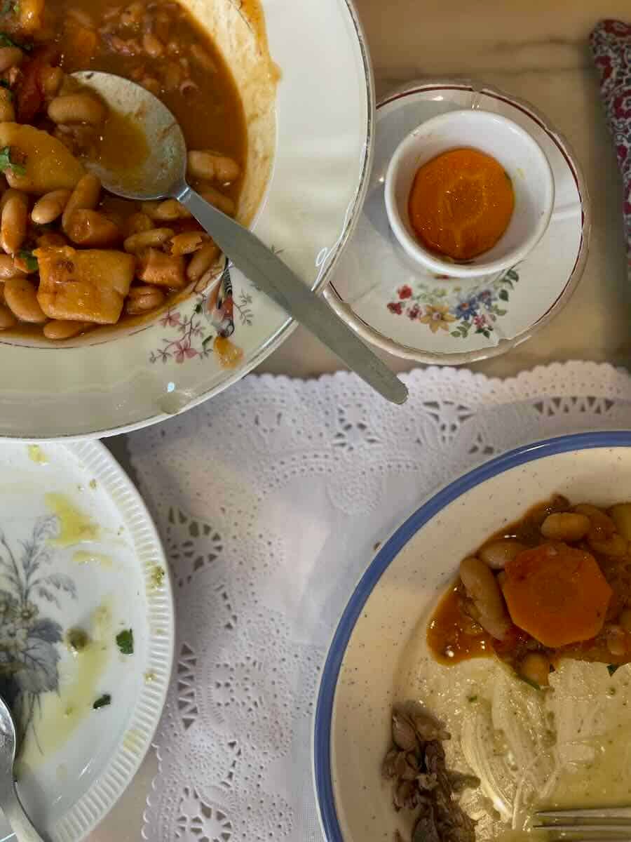 A bowl of hearty bean stew with vegetables and a side of egg yolk, served on a table with a lace tablecloth.