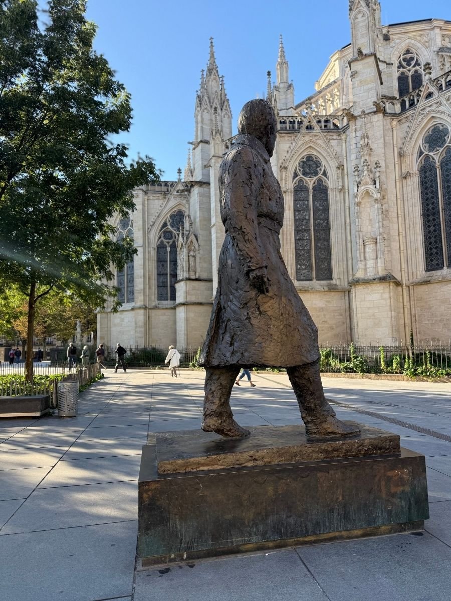 Bronze statue of a walking man in front of the Bordeaux Cathedral in France, with gothic architecture in the background