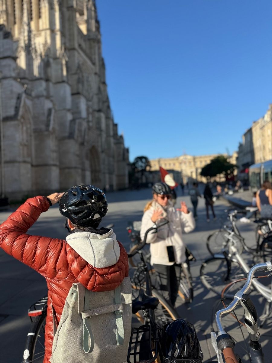 Group on a guided bike tour stopping at Bordeaux Cathedral in France, wearing helmets and admiring the gothic landmark