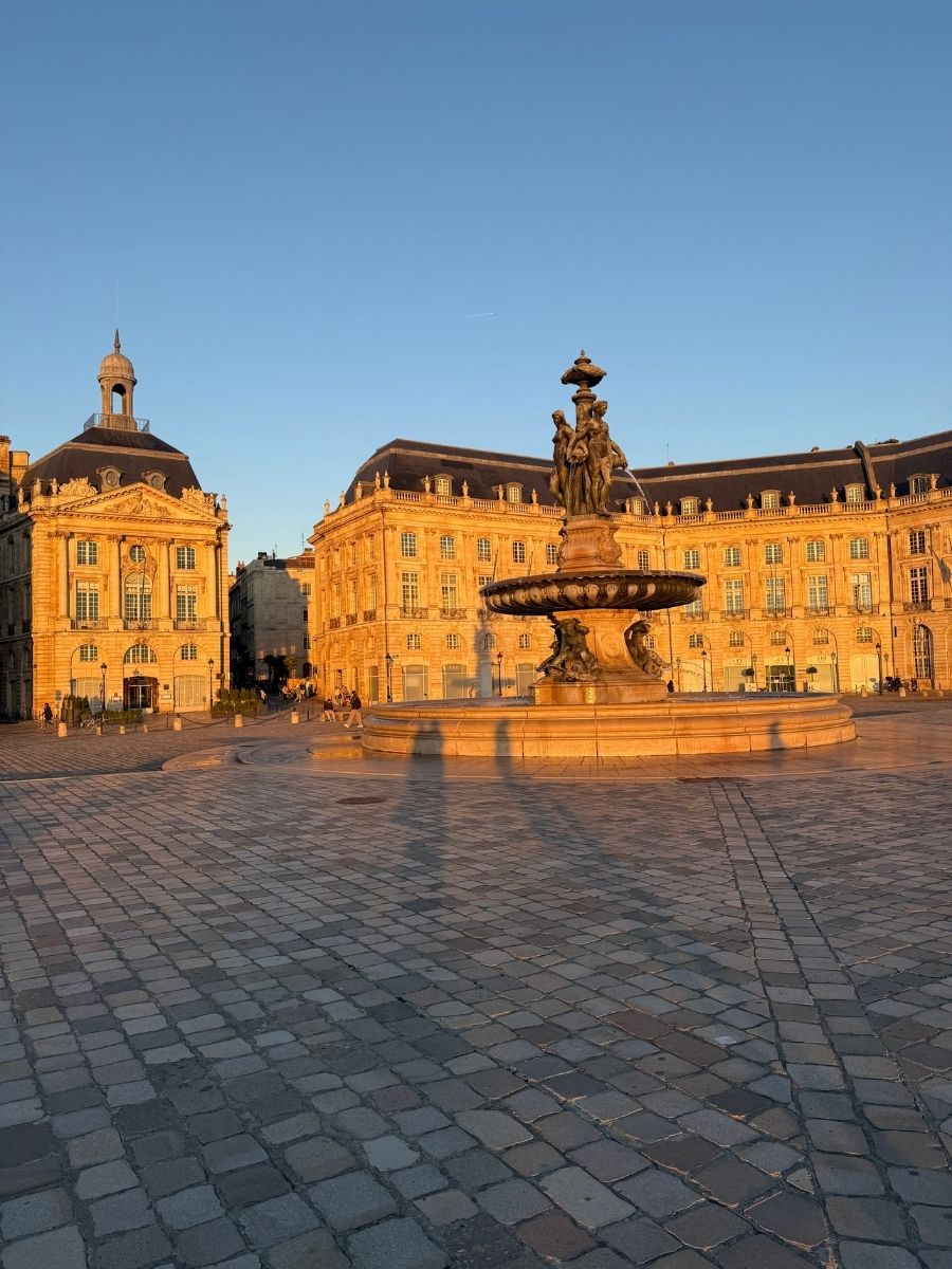 Place de la Bourse in Bordeaux glowing in warm sunlight, with Fountain of the Three Graces in the center