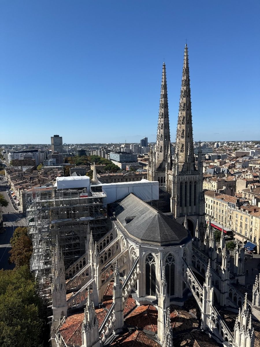 Aerial view of Bordeaux’s Saint-André Cathedral with intricate flying buttresses and twin spires under clear blue skies, showcasing the cityscape of Bordeaux, France.