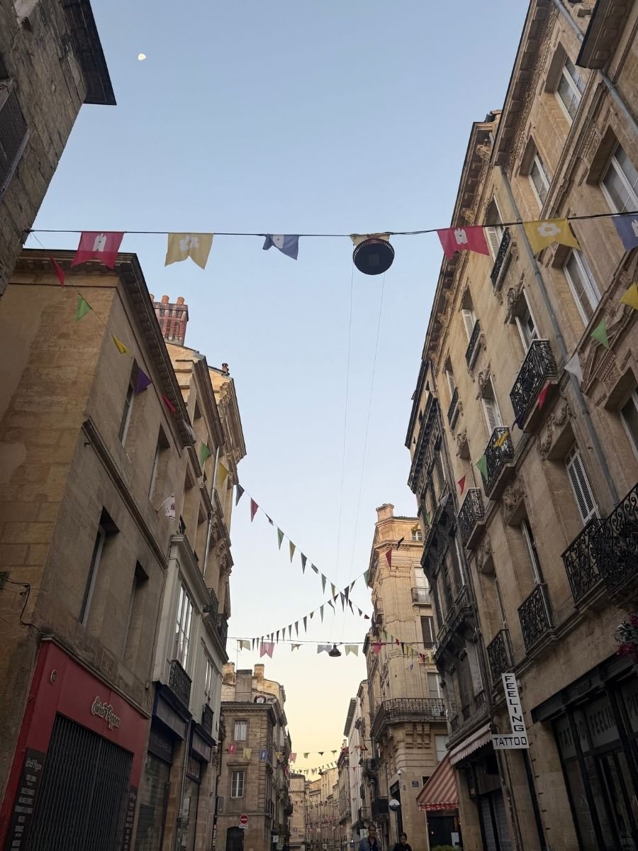 Colorful flags strung above a charming narrow street lined with historic buildings in the heart of Bordeaux, France.