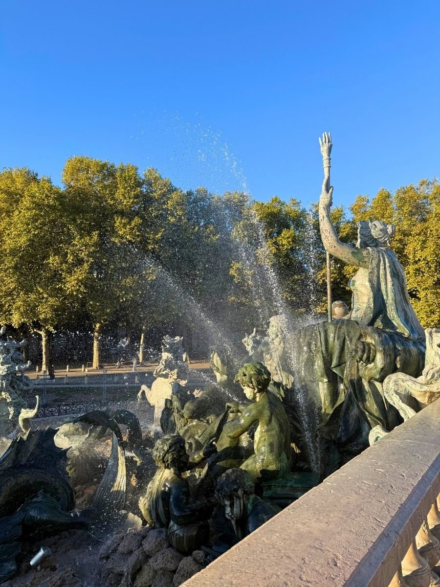 Dramatic fountain scene at the Monument aux Girondins in Bordeaux, France, featuring dynamic bronze statues of mythological figures and sea creatures with water spraying into the air.