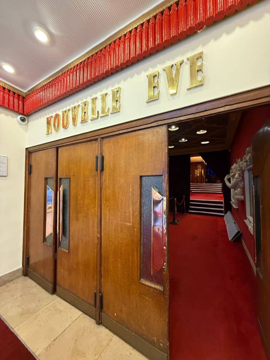 Wooden doors with gold lettering spelling “Nouvelle Eve,” leading into the cabaret’s red-carpeted interior.