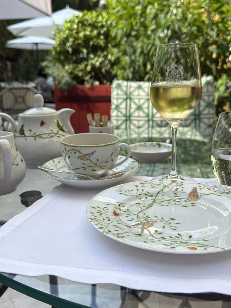 Elegant tea service with floral china, wine glass, and tea set on a sunny garden table.