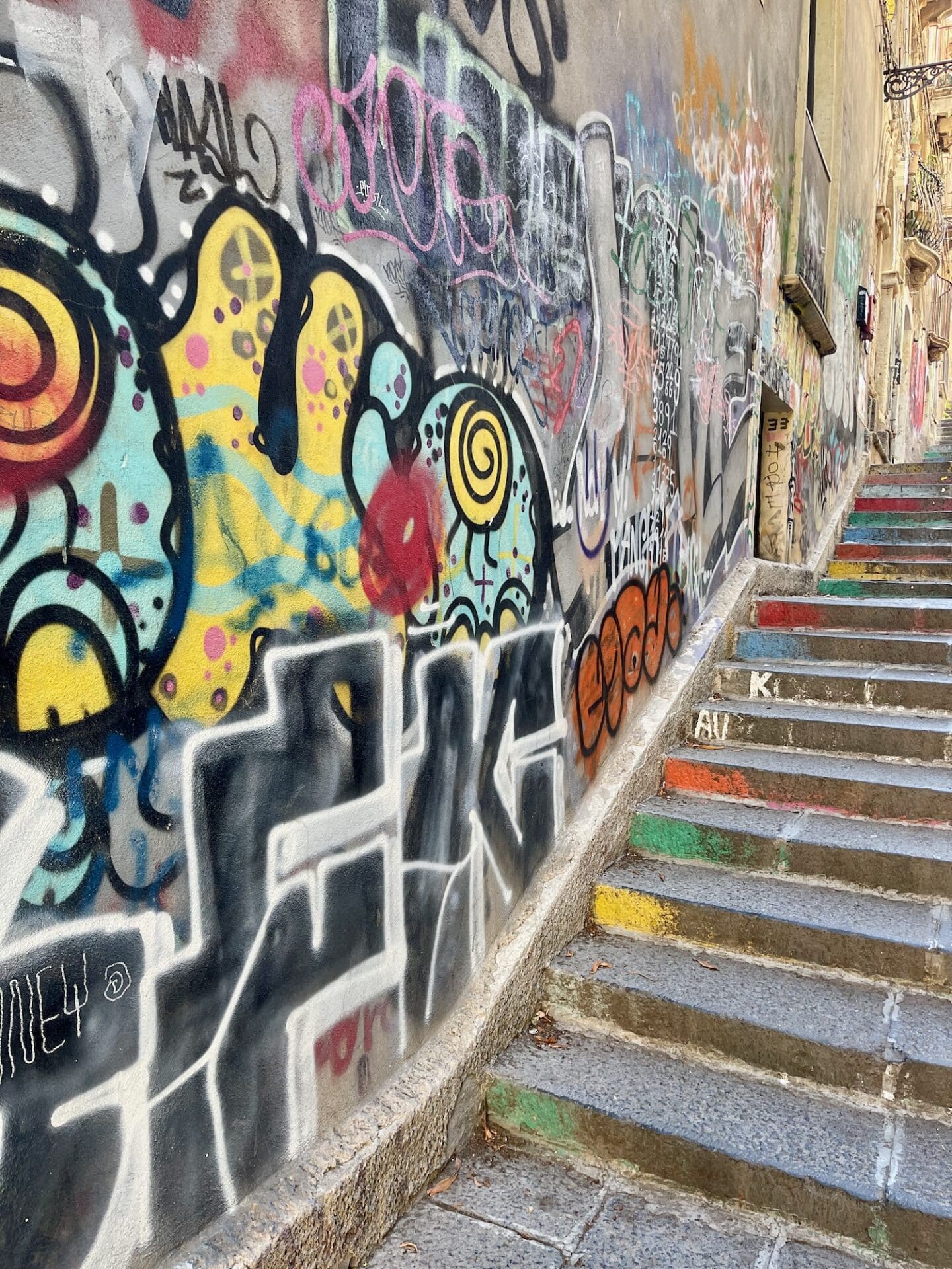 Colorful graffiti on a wall next to a staircase in Catania.