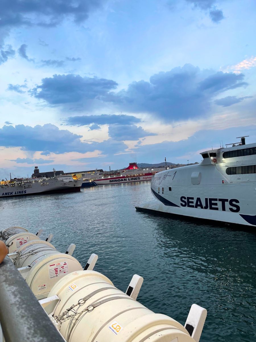 Multiple ferries, including SeaJets, Anek Lines, and Minoan Lines, docked at the Port of Piraeus during sunset.