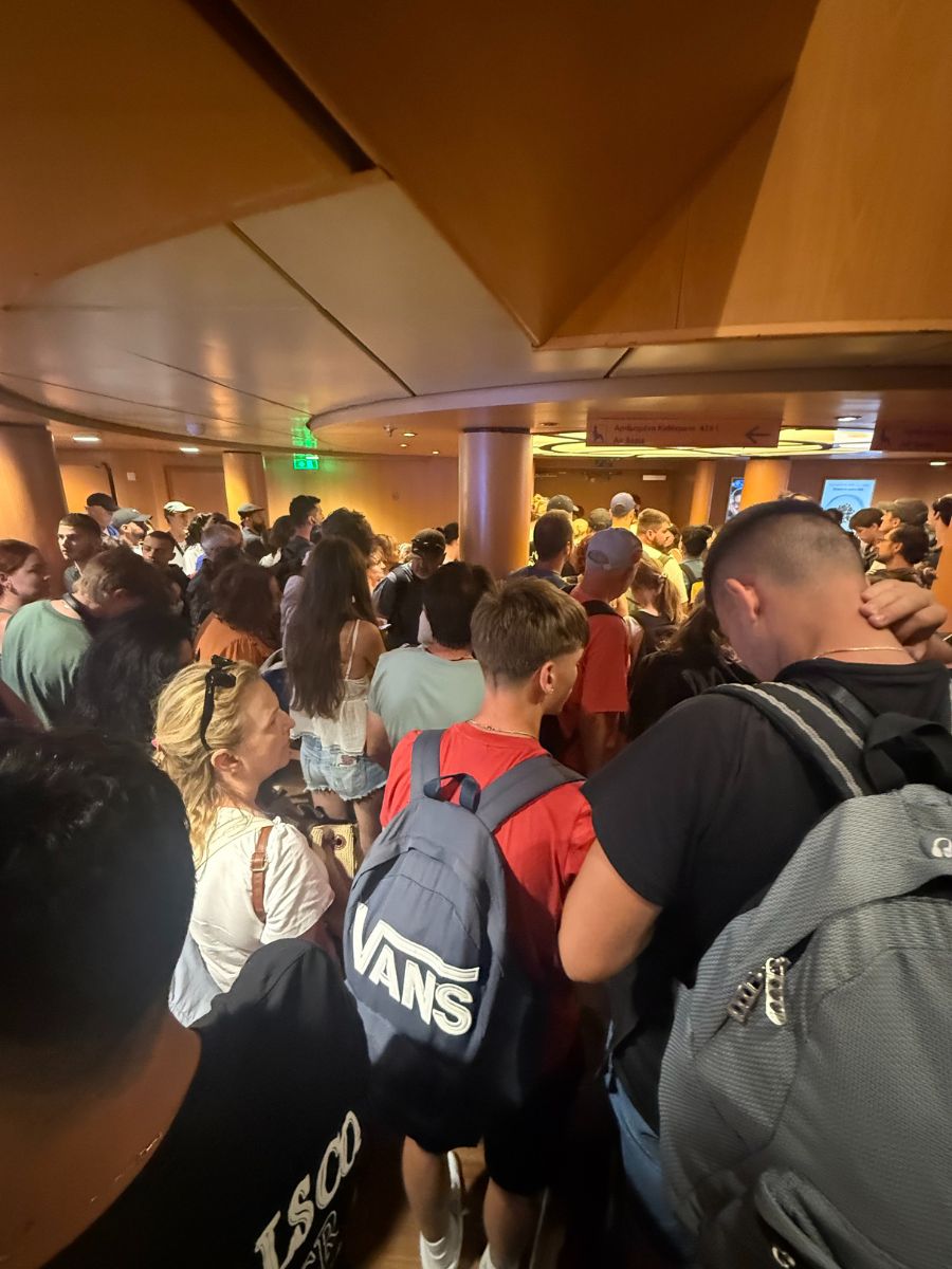 Large crowd of passengers tightly packed inside a Blue Star ferry boarding area, some carrying backpacks.