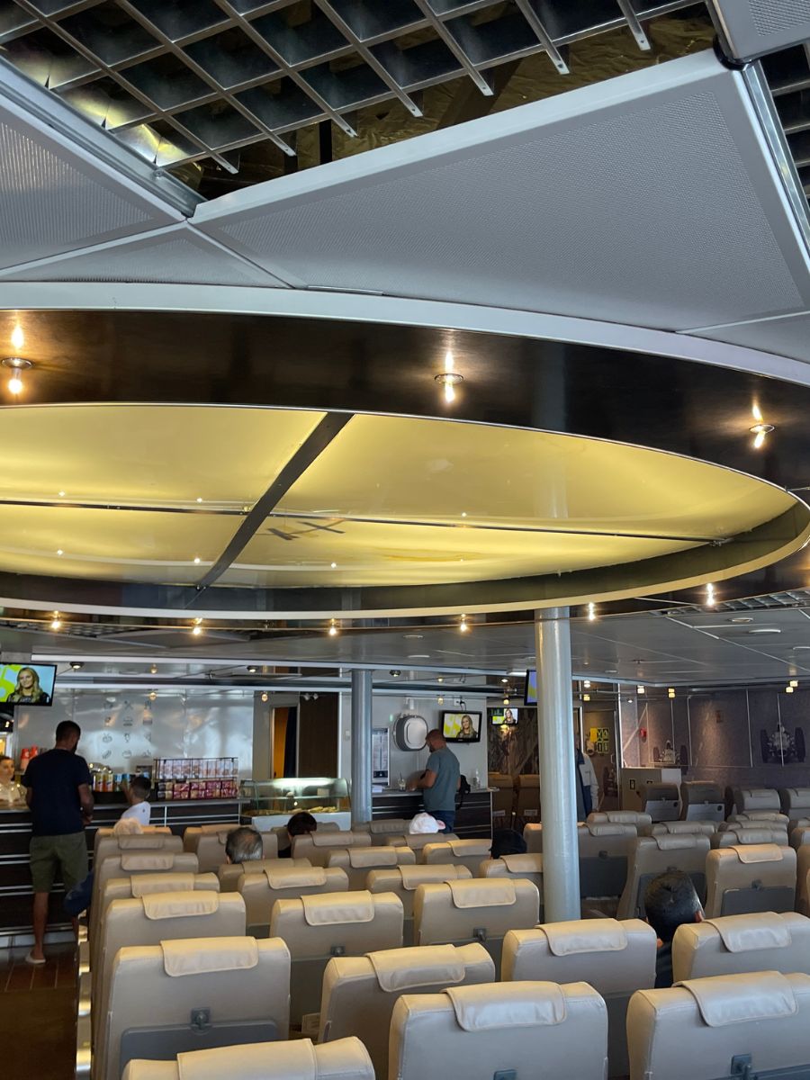 Spacious ferry lounge with cream-colored seats, a snack bar, and passengers waiting comfortably.