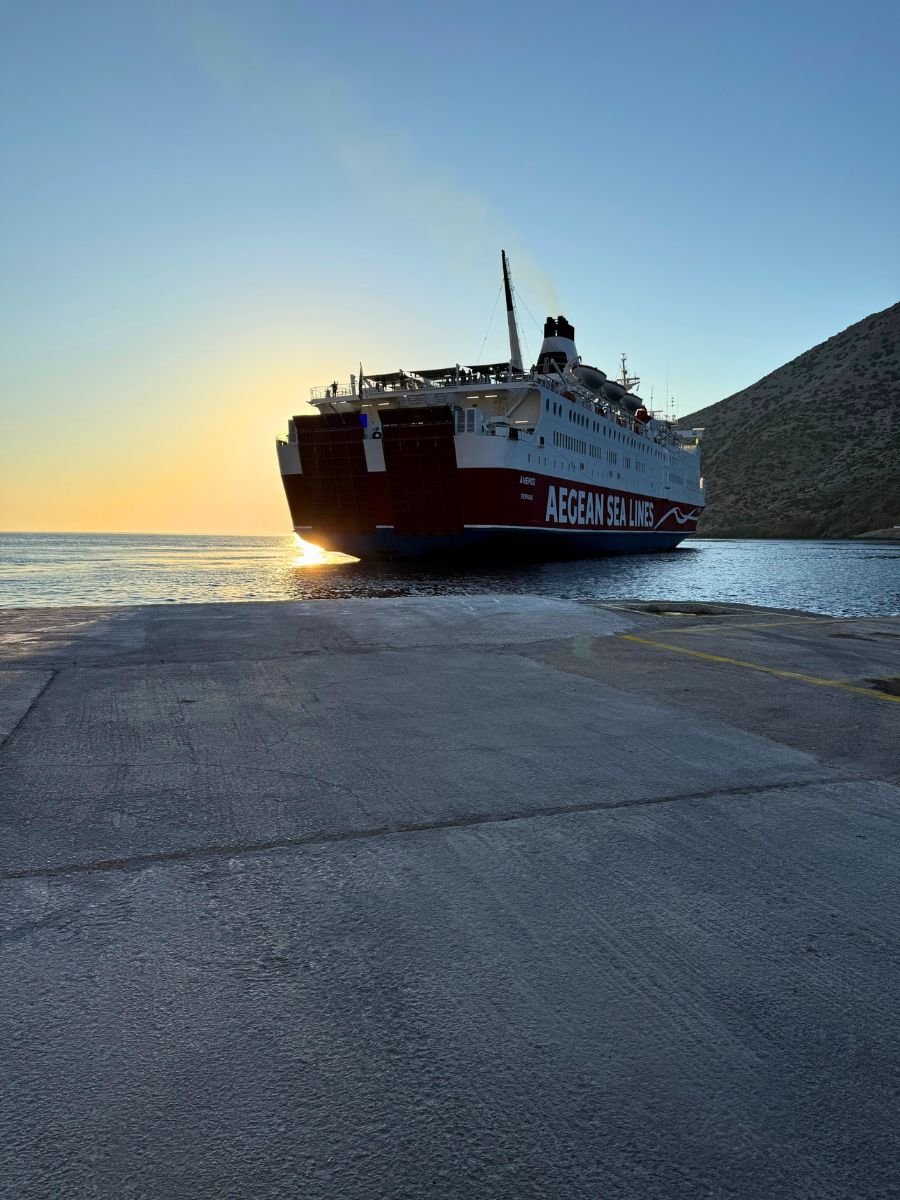 Aegean Sea Lines ferry docked at a port at sunrise, with the sun glowing behind the ship.