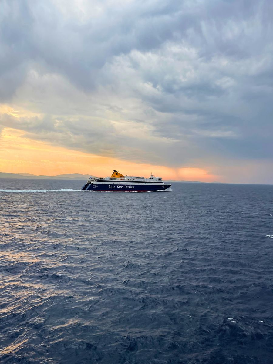Blue Star Ferries ship sailing across the Aegean Sea under a dramatic cloudy sky at sunset.