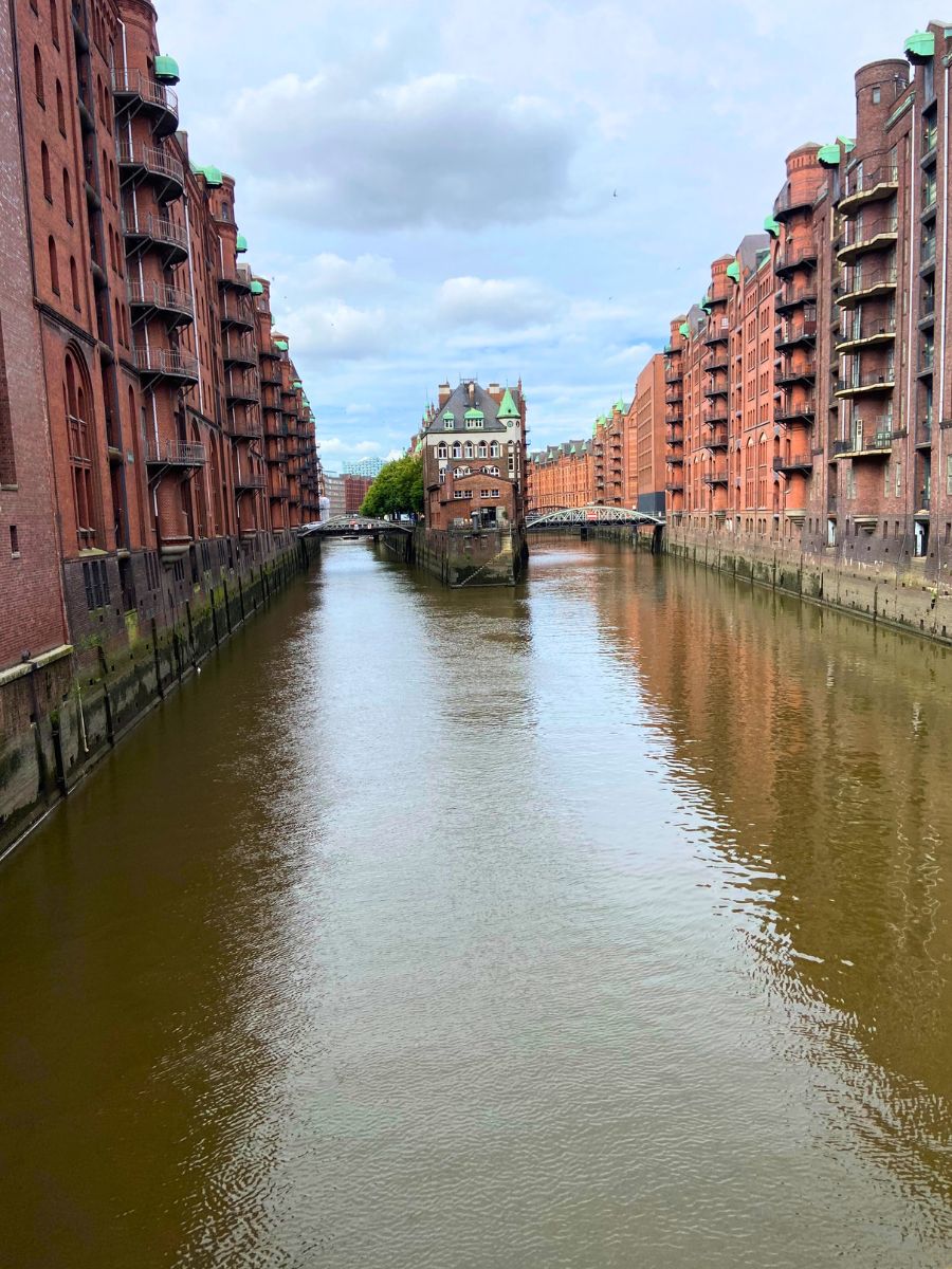 A view of Hamburg’s Speicherstadt, the world’s largest warehouse district, with its iconic red-brick buildings lining the canal. At the center, the famous Wasserschloss stands proudly, making this one of the most photographed spots in the city.