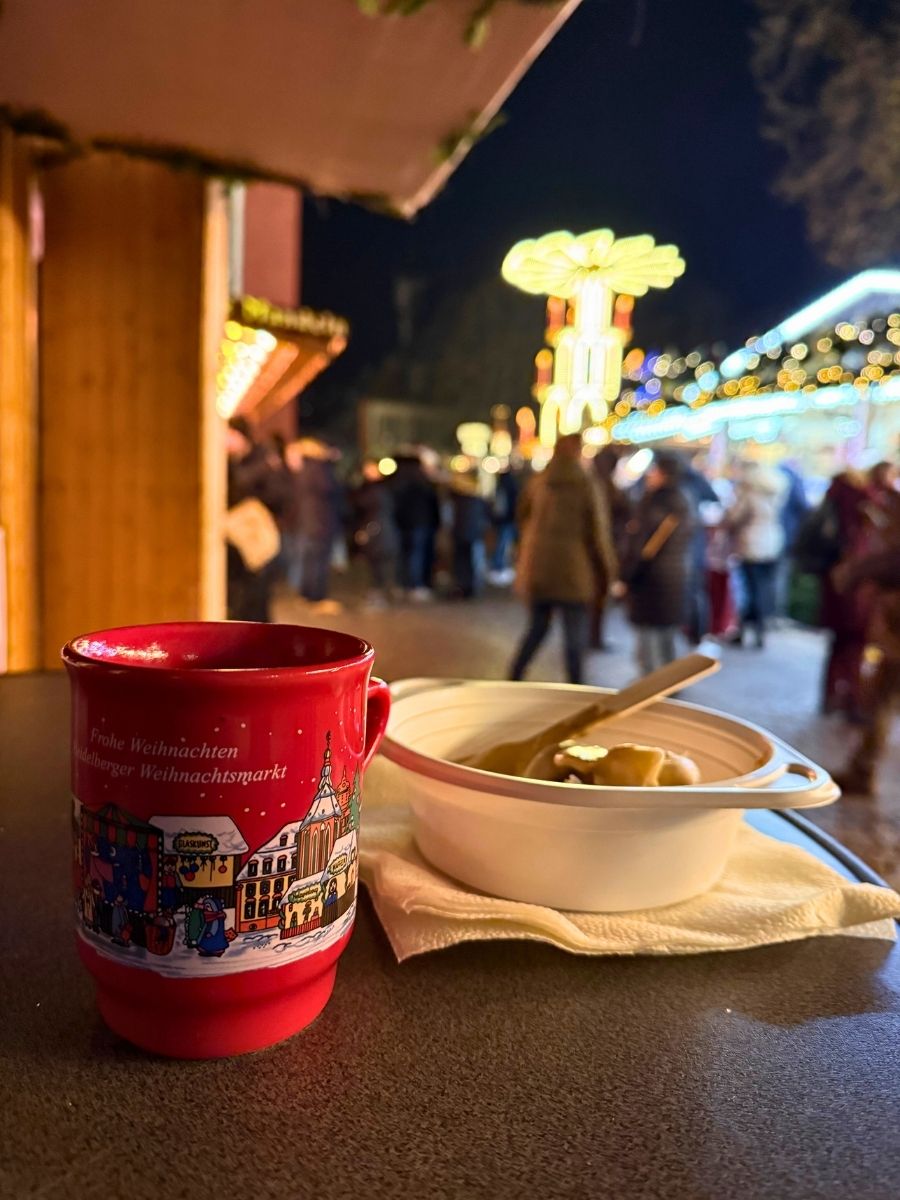 Glühwein and pierogi on table with blurred festive lights and crowd in the background.